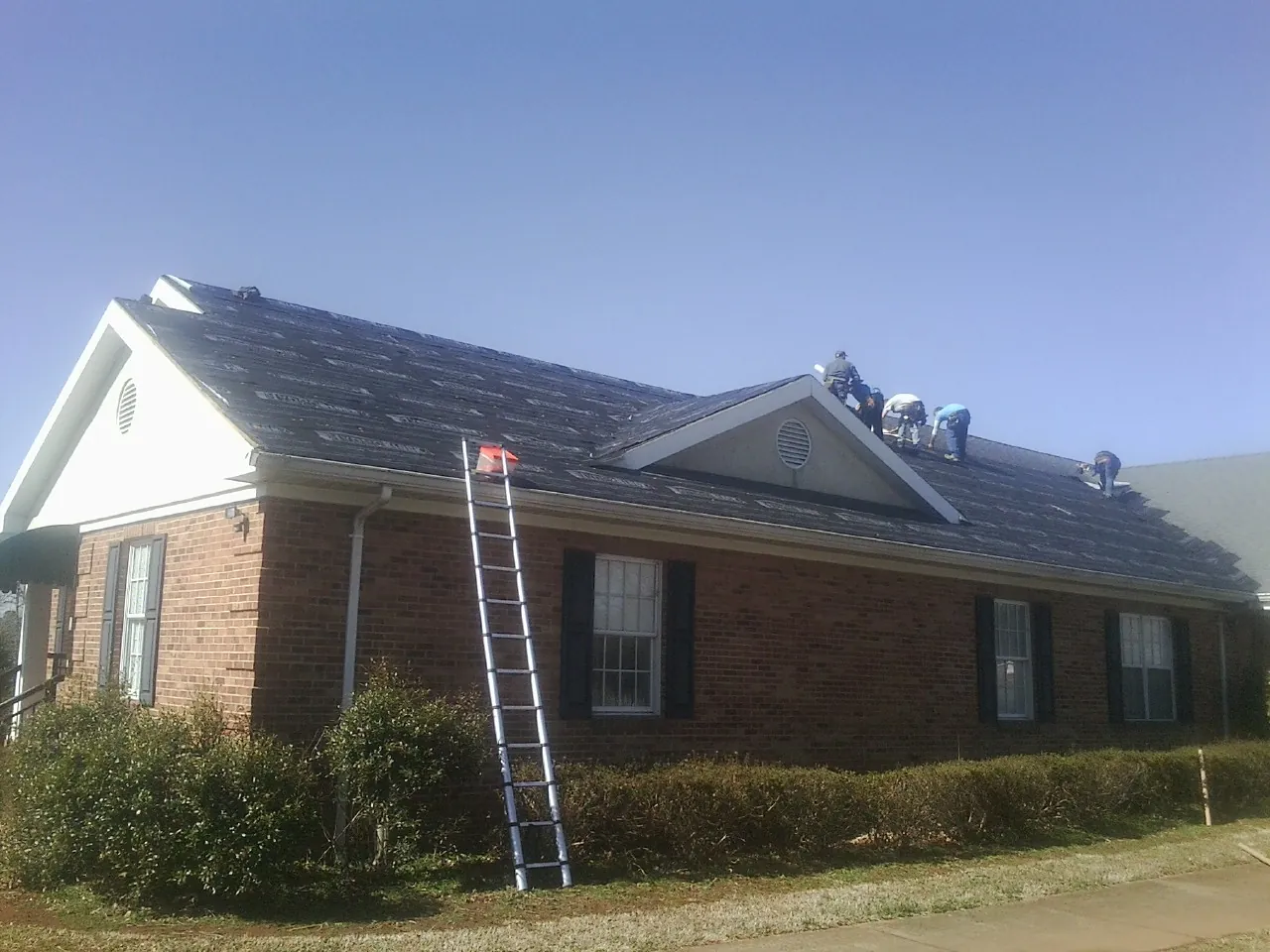 Crew tearing shingles off a brick ranch roof with a ladder set — Metal Roof Repair work by our crew in Hastings On Hudson