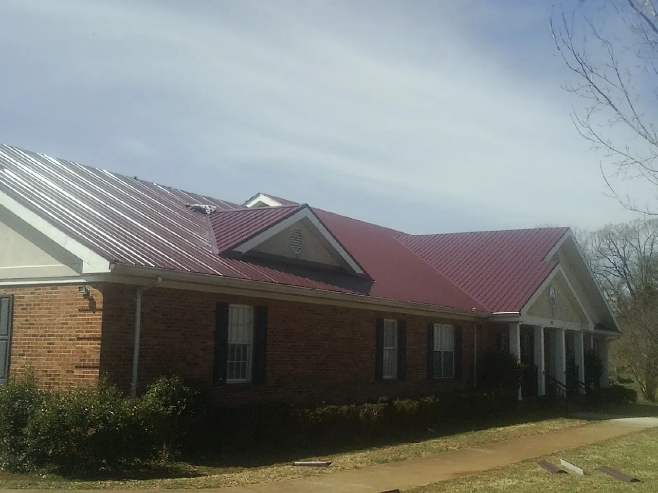 Red metal roof with gabled entries on a long brick building, from a Hail Damage Roof Repair job in Hastings On Hudson