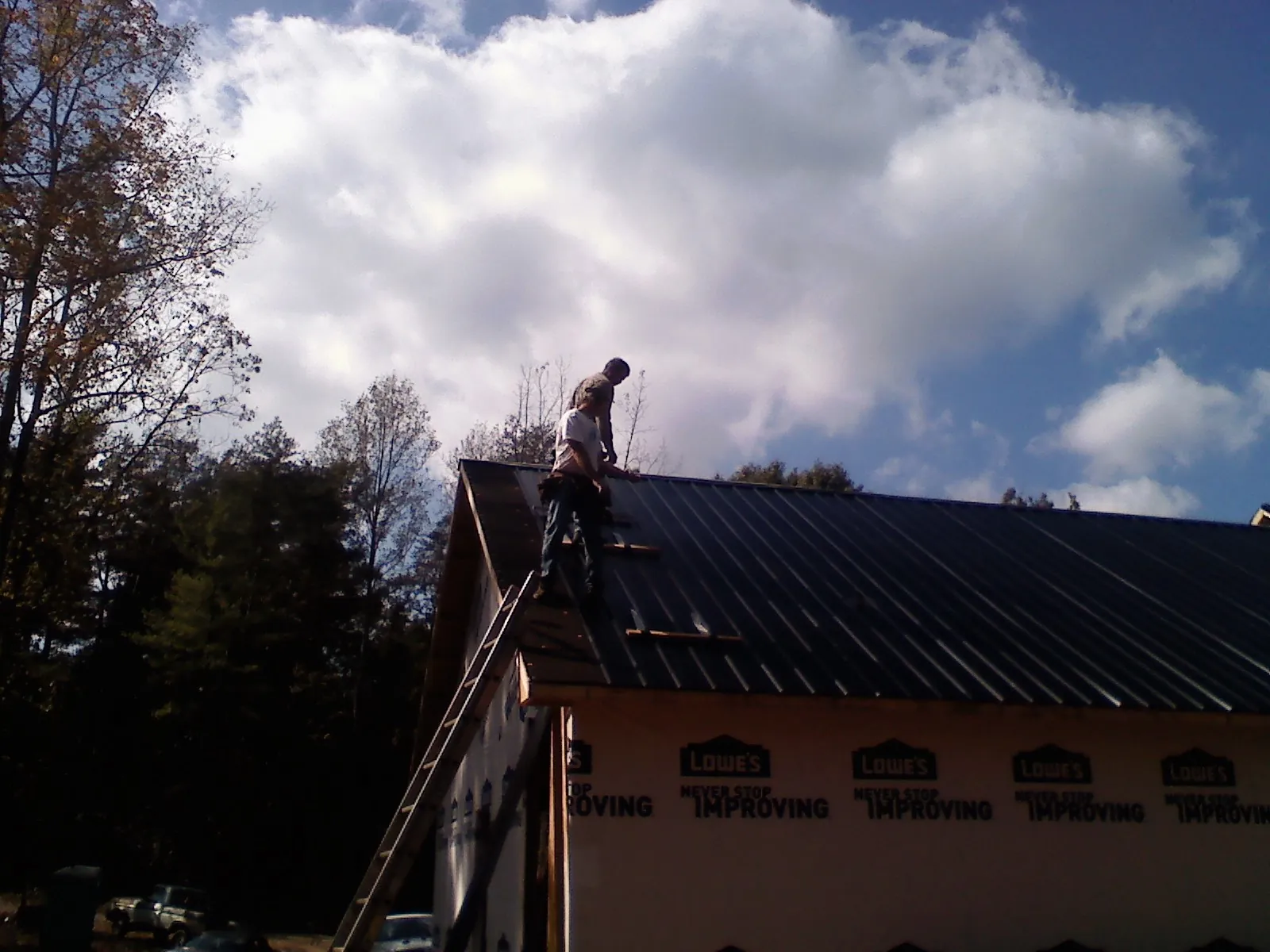 Roofer fastening dark metal panels high against a cloudy sky, from a Roof Inspection job in Hastings On Hudson