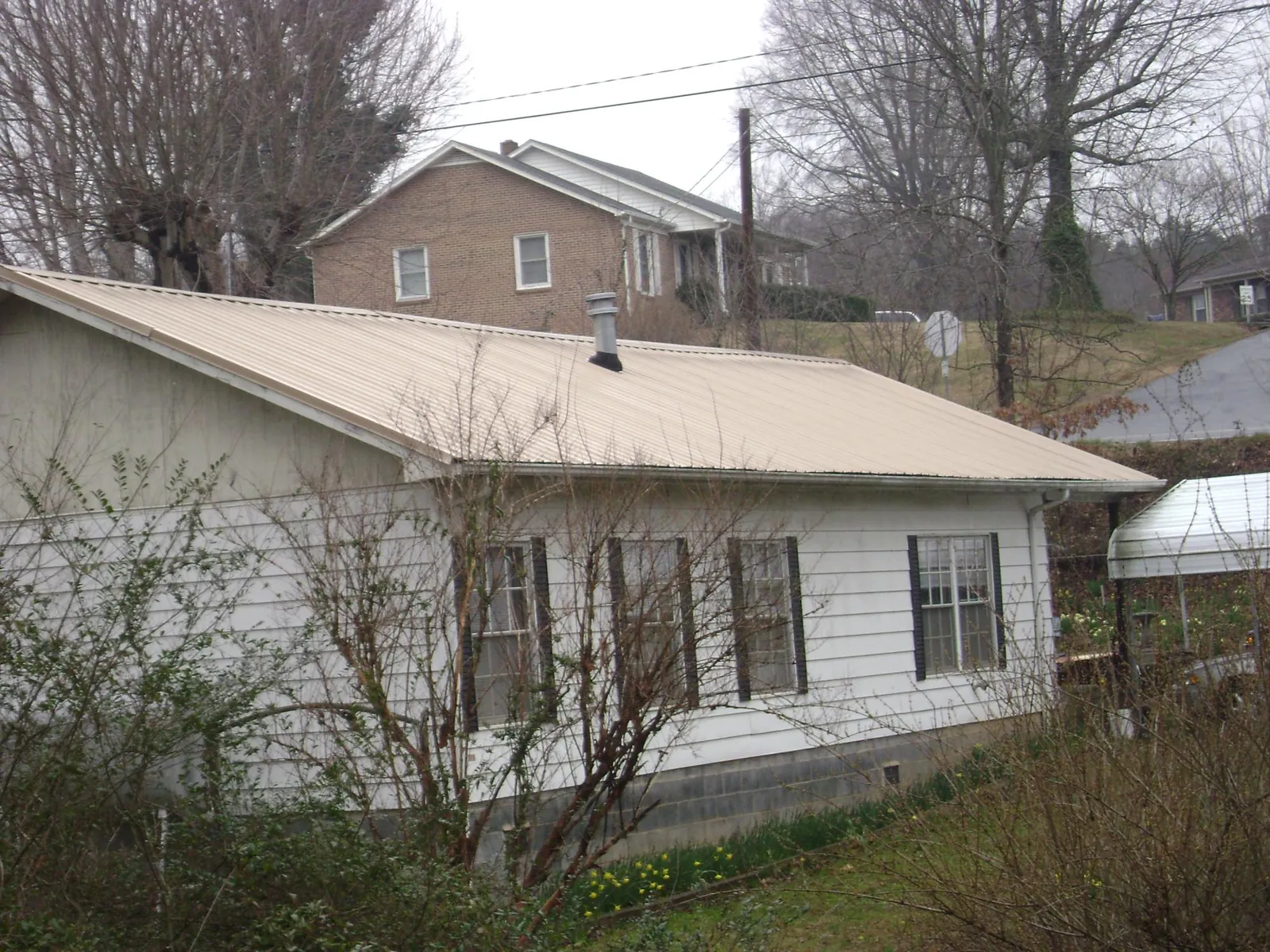 Tan metal roof on a white sided house set into a hillside — Commercial Roofing by Roofing Brothers in Hastings On Hudson